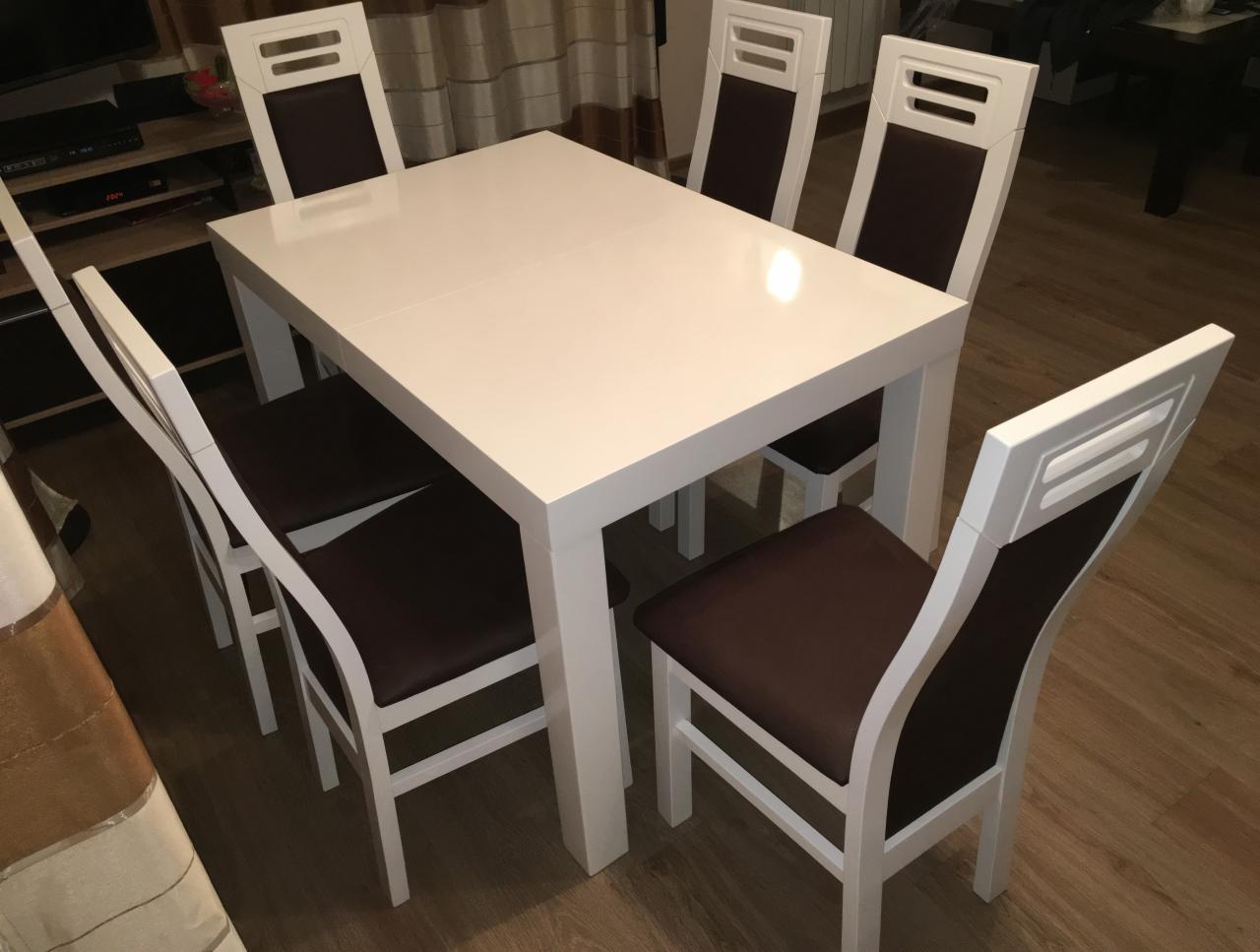 Rozkładany stół z białym blatem i sześcioma krzesłami z brązowymi siedziskami i oparciami, widok z boku, oświetlenie mieszane.