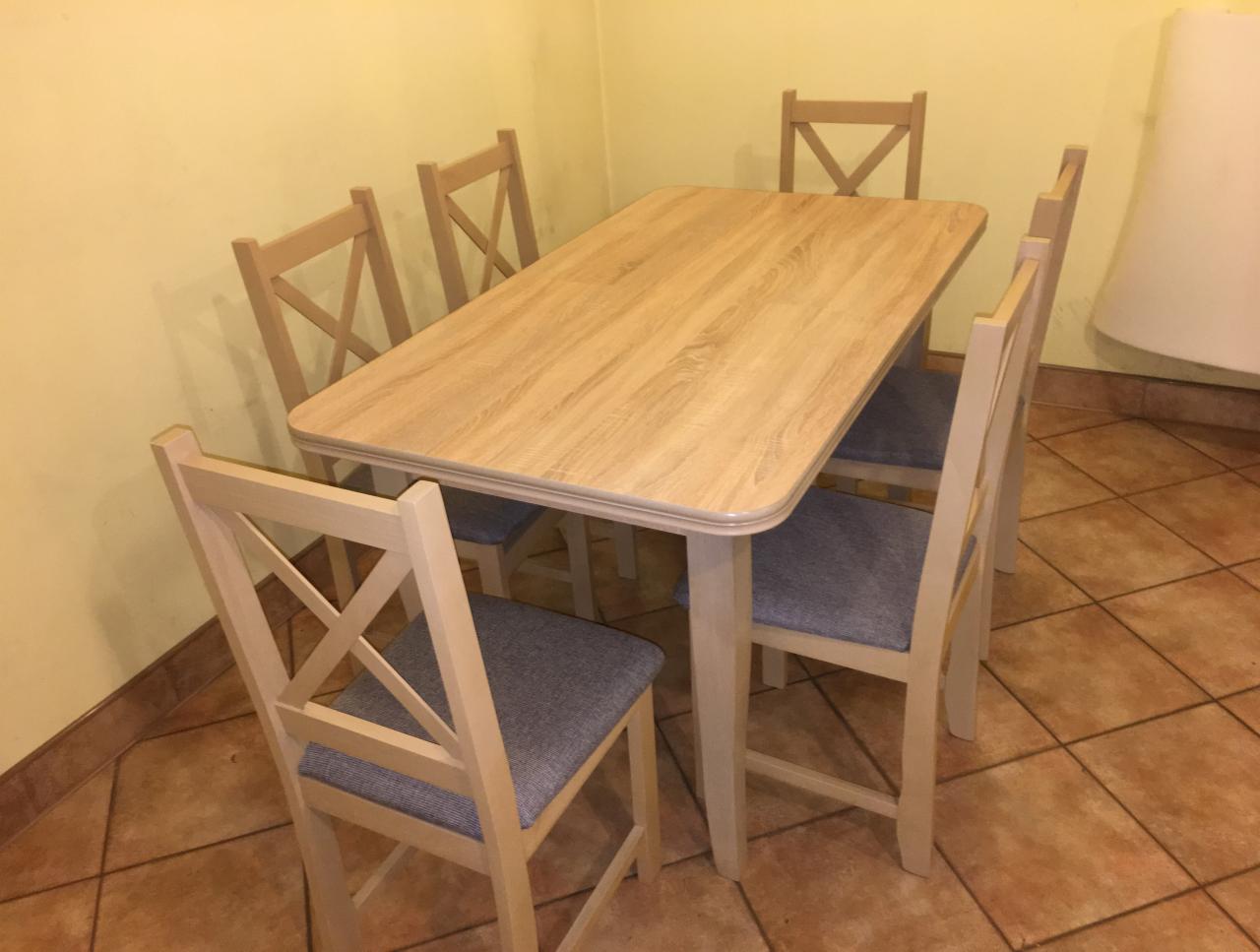 Jasny drewniany stół z zaokrąglonymi krawędziami i sześcioma krzesłami z szarymi siedziskami w żółtym pokoju z brązową podłogą.