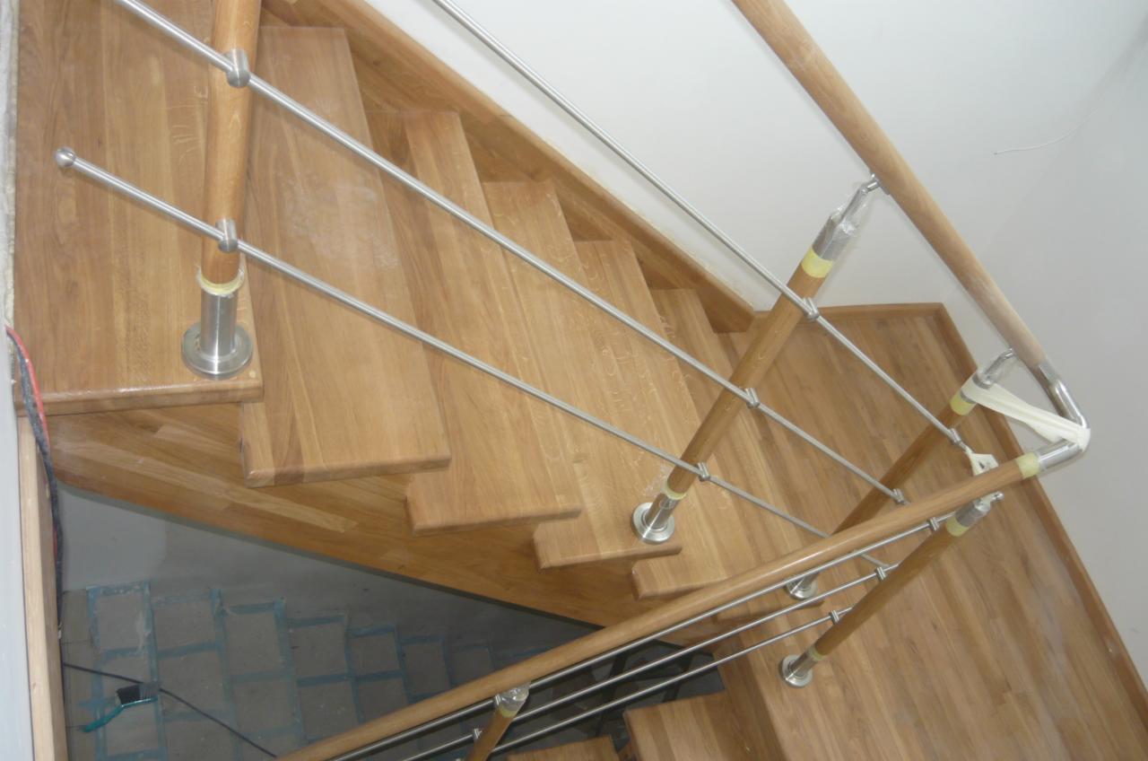 Drewniane schody z metalową balustradą, widok z góry, zabezpieczone taśmą ochronną w miejscu łączeń.