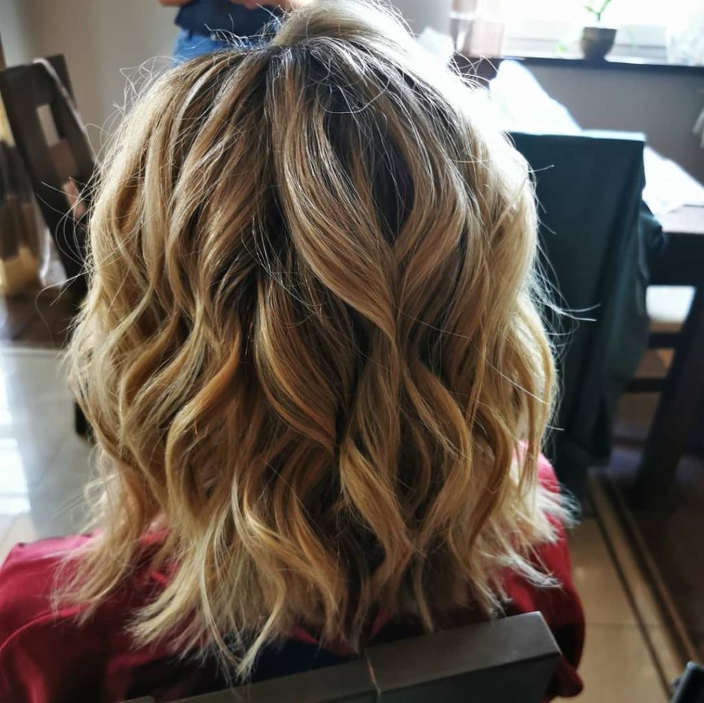 Tył głowy kobiety z blond włosami w stylu beach waves, z widocznymi refleksami i delikatnym cieniowaniem.