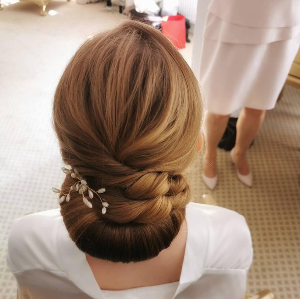 Upięcie ślubne z włosów blond, z wpiętą ozdobą z koralików, widok z tyłu, w tle fragment sukienki i białe szpilki.