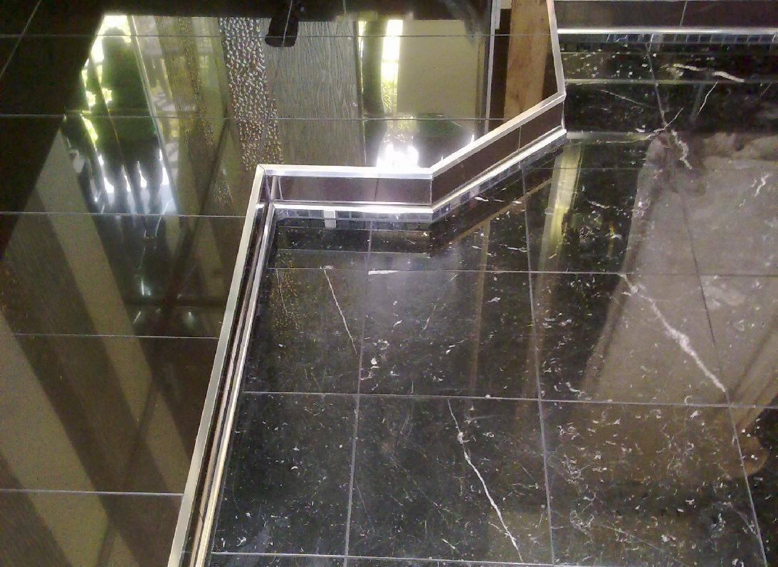 Błyszczące, czarne płytki marmurowe na podłodze i schodach z metalowym wykończeniem krawędzi, odbijające światło.