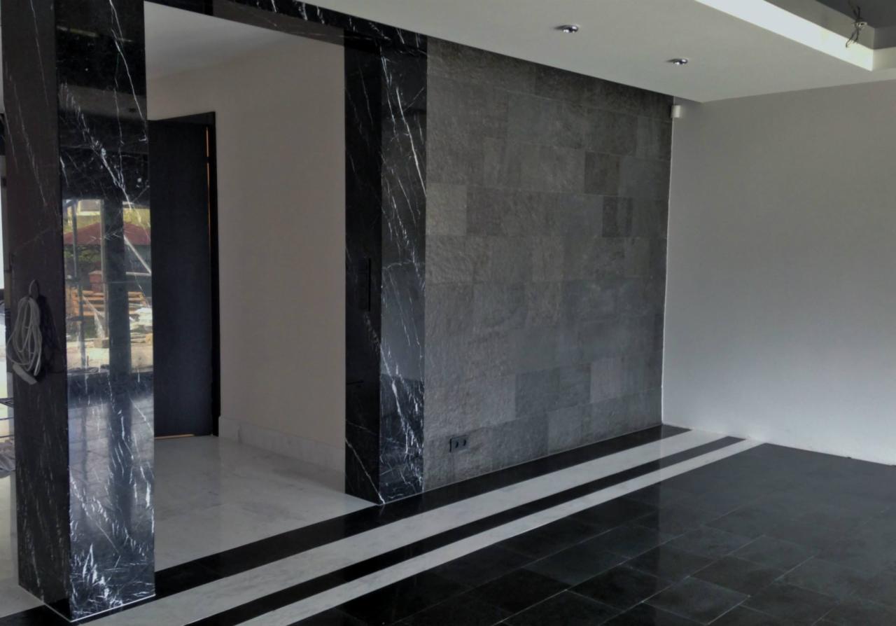 Wnętrze z kamienną ścianą z szarego łupka, marmurowe filary i podłoga z czarno-białych płytek tworzących pasy, nowoczesny design.