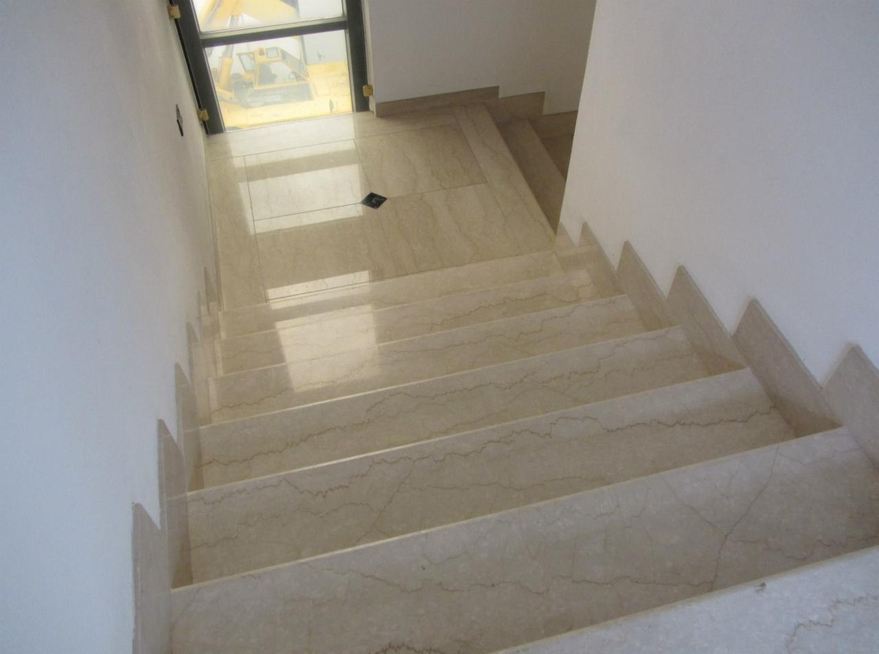 Widok z góry na wykończone, jasne schody z kamienia naturalnego z widocznym oknem i sprzętem budowlanym na zewnątrz.