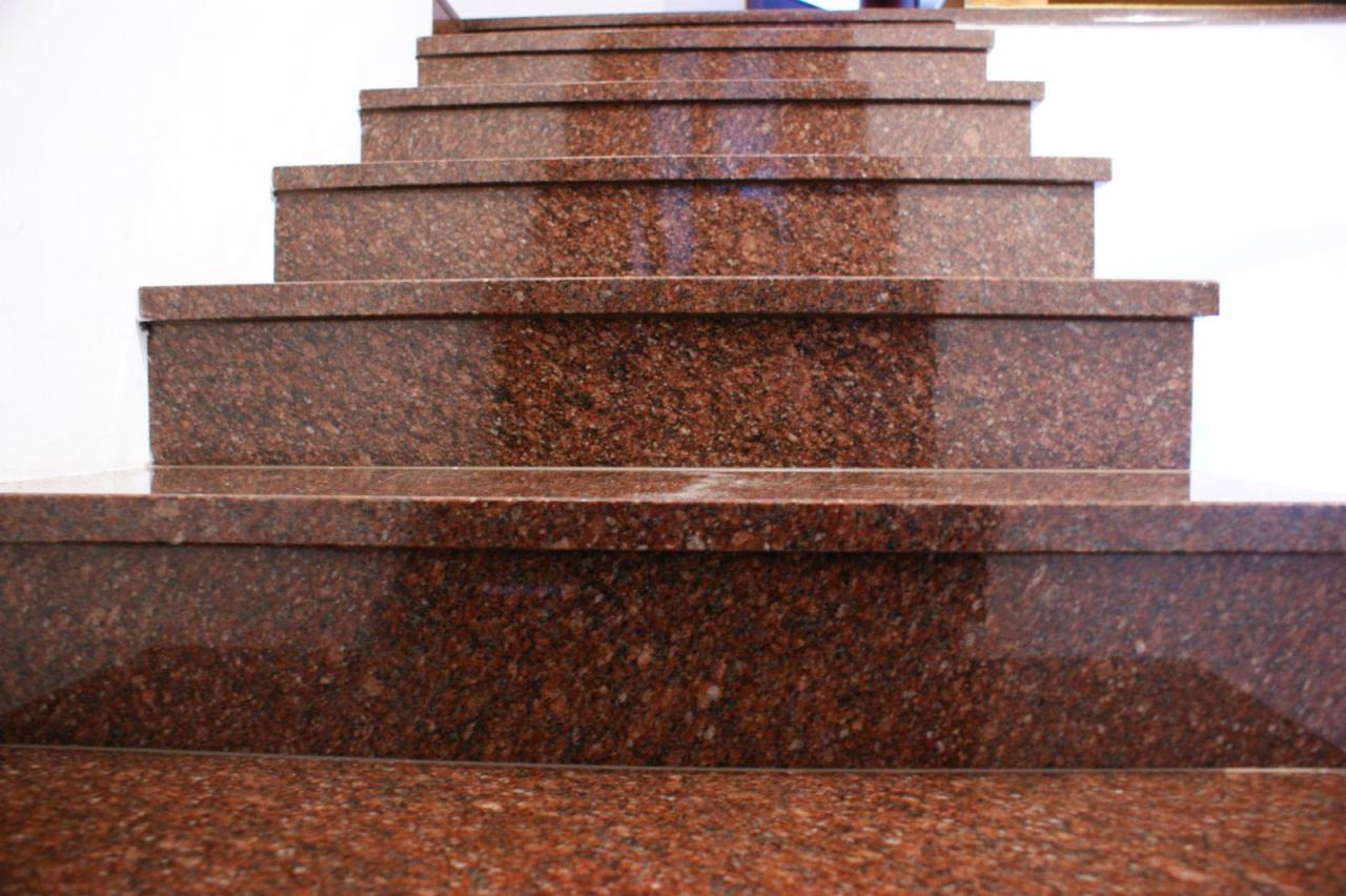 Schody wewnętrzne wykończone czerwonym granitem o ziarnistej strukturze, widok z dołu ukazujący stopnie i podstopnice, minimalizm w wykończeniu.