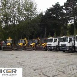 Park maszyn budowlanych firmy Lenker Grupa Aquanet: pomarańczowa koparka Daewoo, rząd żółtych koparko-ładowarek i białe ciężarówki MAN z logo firmy na tle drzew