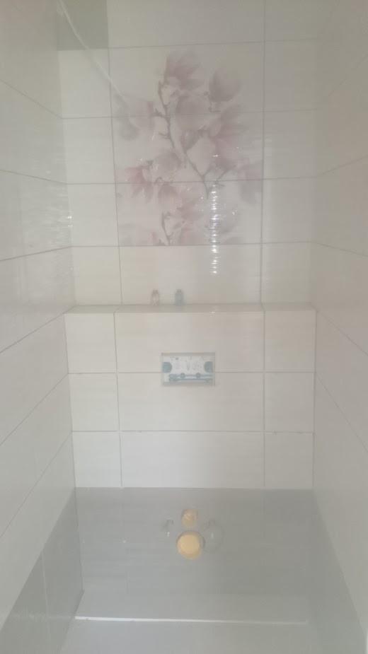 Wykończona łazienka z jasnymi płytkami, w tym z motywem kwiatowym na ścianie, widoczna instalacja podtynkowa WC i odpływ liniowy.