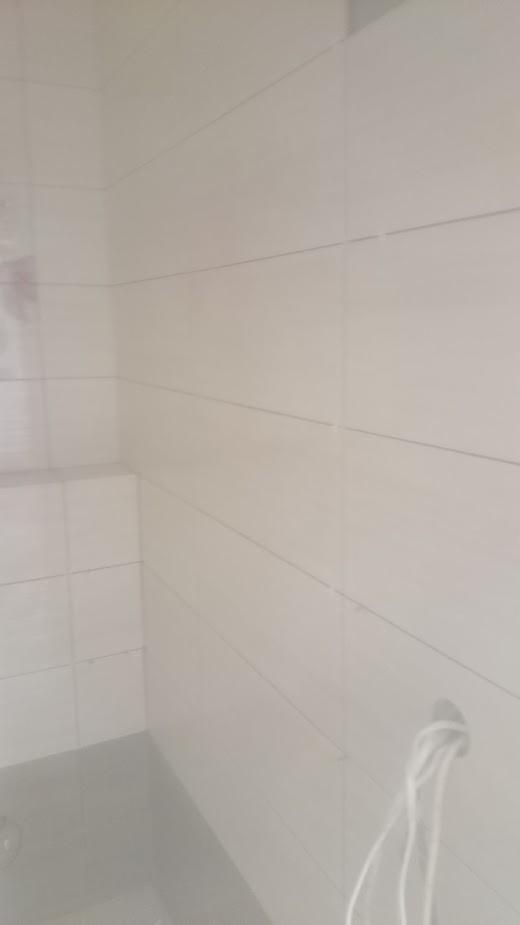 Wyłożona białymi, podłużnymi płytkami ściana w łazience, widoczne fugi i otwór na przewody elektryczne.