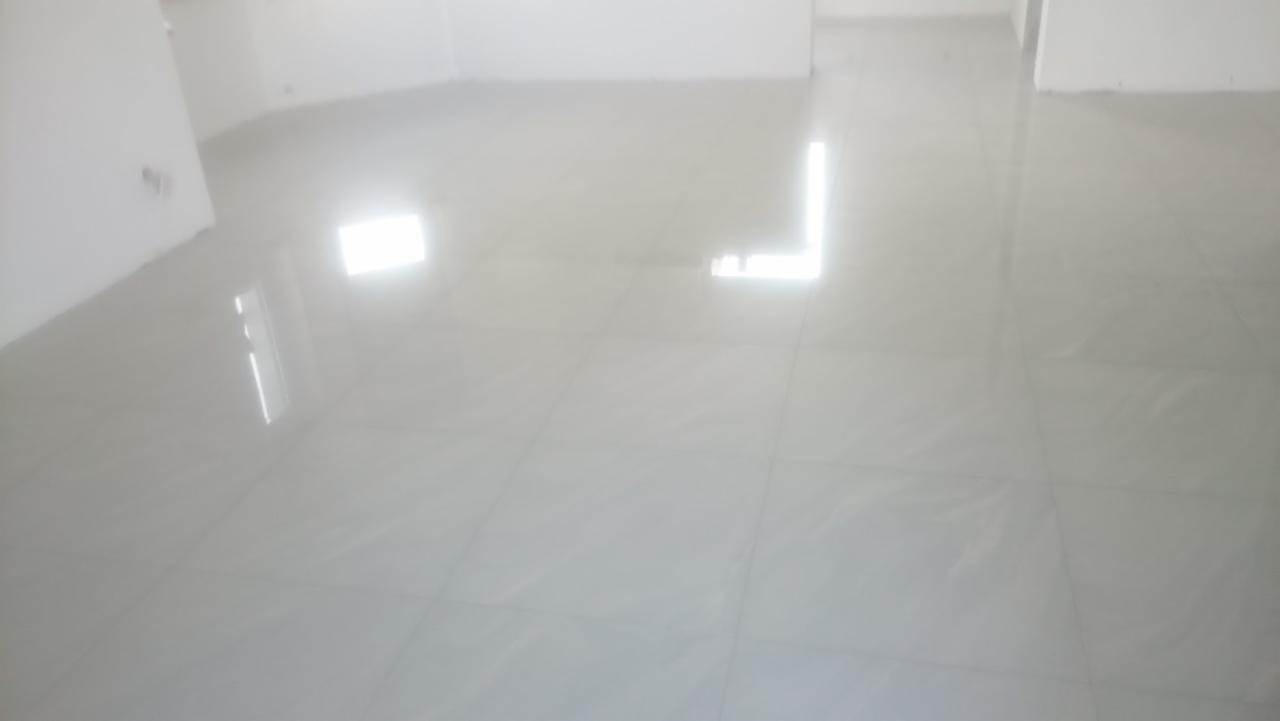 Błyszcząca, jasnoszara podłoga z płytek ceramicznych w pustym, świeżo wyremontowanym pomieszczeniu, odbijająca światło okien.