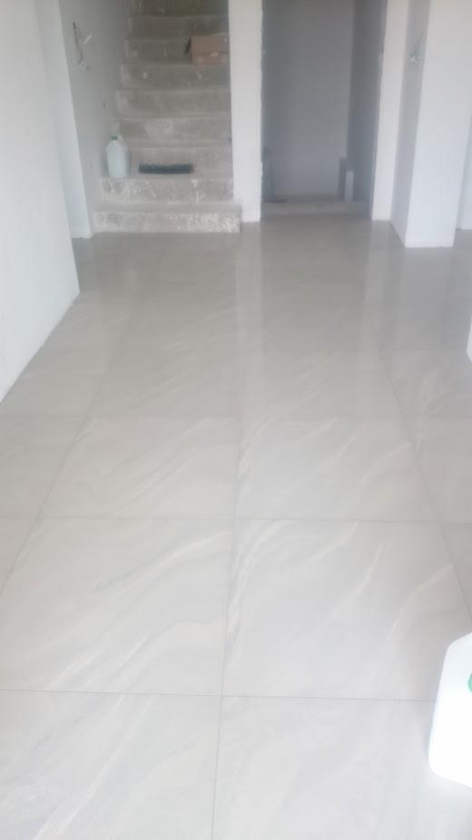 Wykończona podłoga z jasnych, błyszczących płytek imitujących marmur w nowym, pustym pomieszczeniu z surowymi schodami w tle.