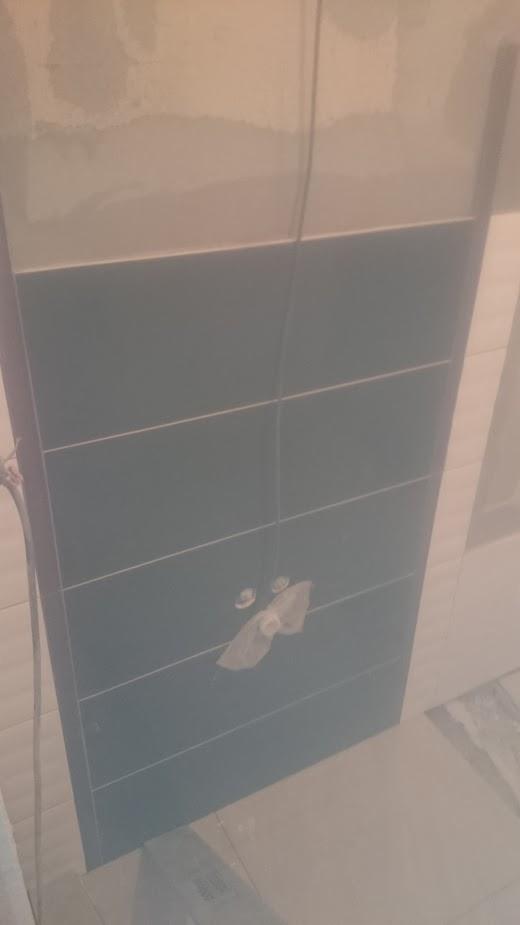 Ściana w trakcie układania płytek, widoczne niebieskie płytki oraz zabezpieczone rury wodne.