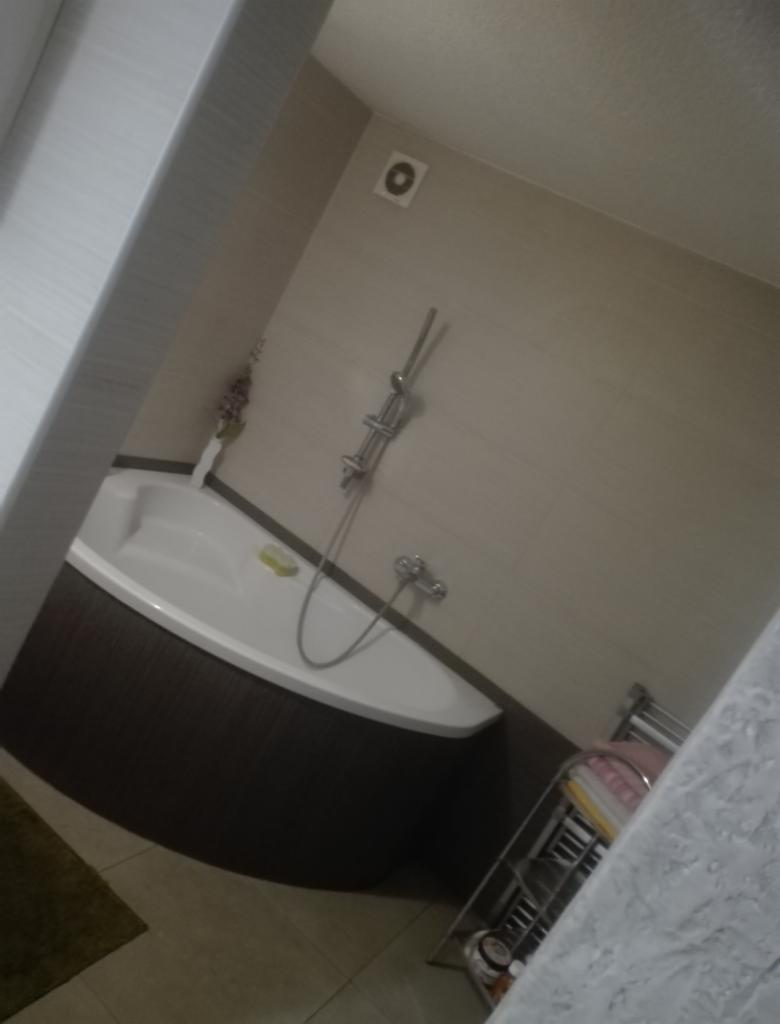 Narożna wanna obudowana ciemnobrązowymi płytkami w łazience z beżowymi ścianami, widoczna armatura i akcesoria łazienkowe.