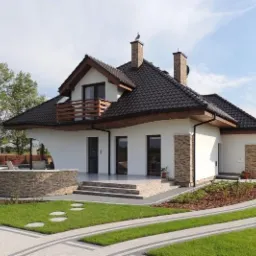 Gotowy dom murowany z brązowym dachem i jasną elewacją w Orzechowie, z widocznym tarasem i ścieżką z kostki brukowej prowadzącą do domu.