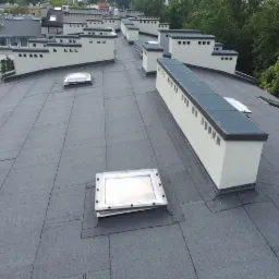 Wykończony dach kamienicy w Warszawie pokryty papą termozgrzewalną z licznymi świetlikami i kominami wentylacyjnymi, widok z góry.