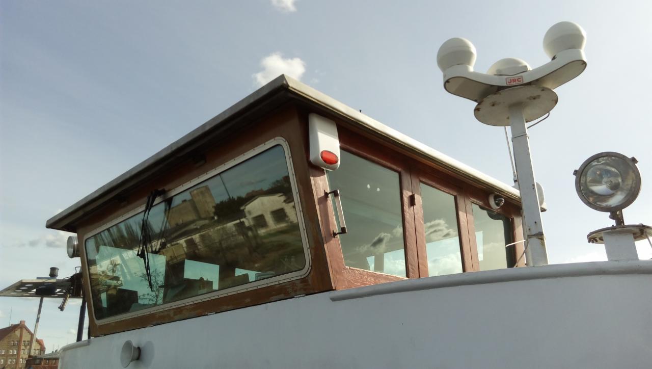 Kabina sterownicza kutra rybackiego z widoczną instalacją alarmową i monitoringiem, kamera umieszczona na zewnątrz, widok na budynki odbijające się w szybach.