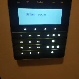 Panel sterowania alarmem Satel z podświetlonym ekranem wyświetlającym komunikat 'Ustaw zegar !', widoczne przyciski numeryczne i funkcyjne.