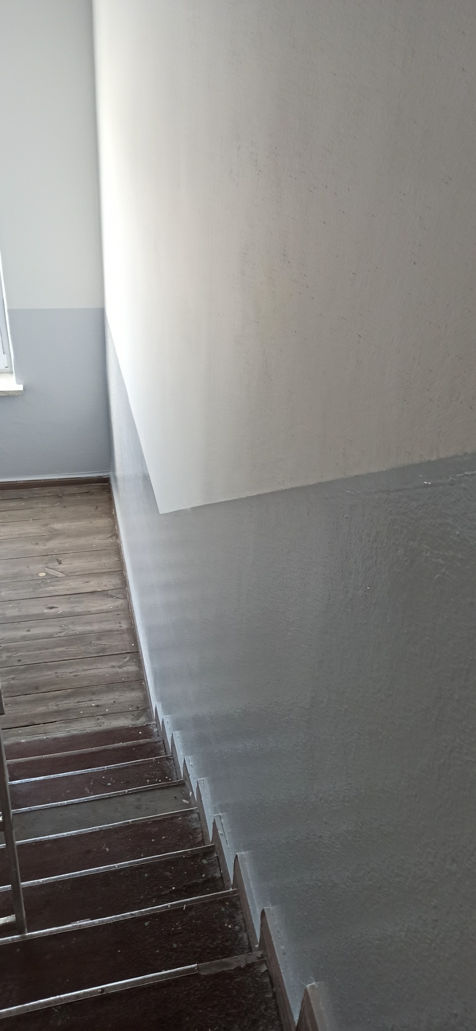 Świeżo pomalowana klatka schodowa z szarą lamperią i białymi ścianami powyżej, widoczne drewniane schody z metalowymi listwami antypoślizgowymi.