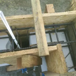 Szczegółowy widok z góry na szalunek z płyty OSB i zbrojenie z prętów stalowych, przygotowany do zalania betonem, widoczna rurka osłonowa na przewody.