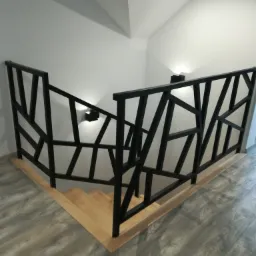Nowoczesna, czarna balustrada schodowa o geometrycznym wzorze, zamontowana na drewnianych schodach w jasnym wnętrzu z szarą podłogą imitującą drewno.