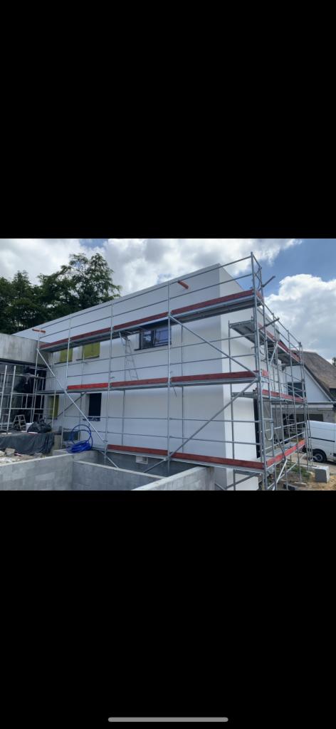 Nowoczesny dom w Grzegorzewie z białą elewacją, otoczony rusztowaniami, widoczne okna z żółtymi foliami ochronnymi oraz niezabudowany jeszcze teren wokół.