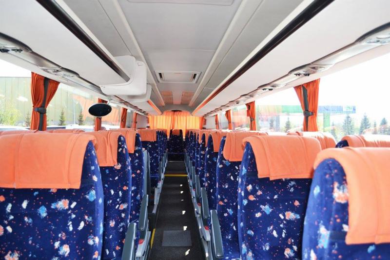 Wnętrze autobusu turystycznego z rzędami niebieskich siedzeń w kwiaty i pomarańczowymi zagłówkami, widok z perspektywy przejścia.