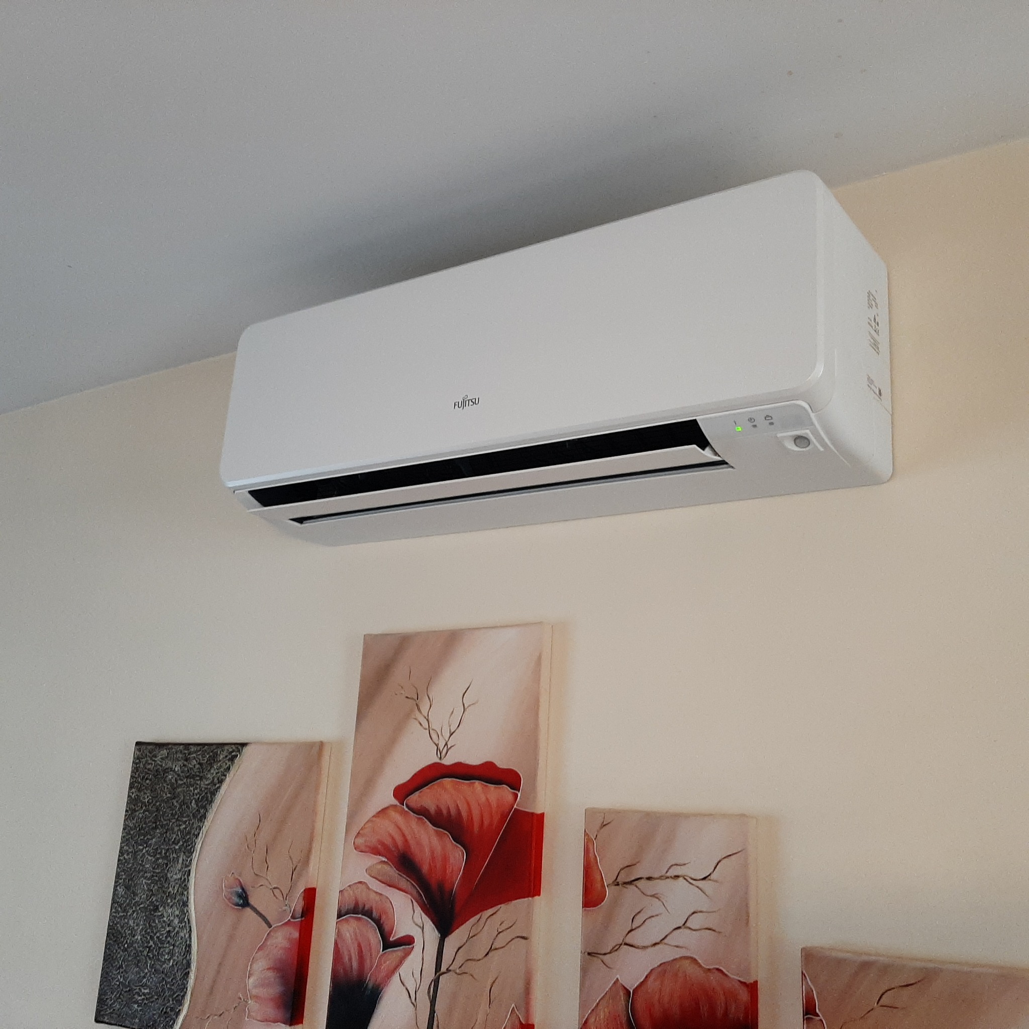 Biały klimatyzator Fujitsu zamontowany na ścianie w pomieszczeniu z obrazami przedstawiającymi czerwone maki.