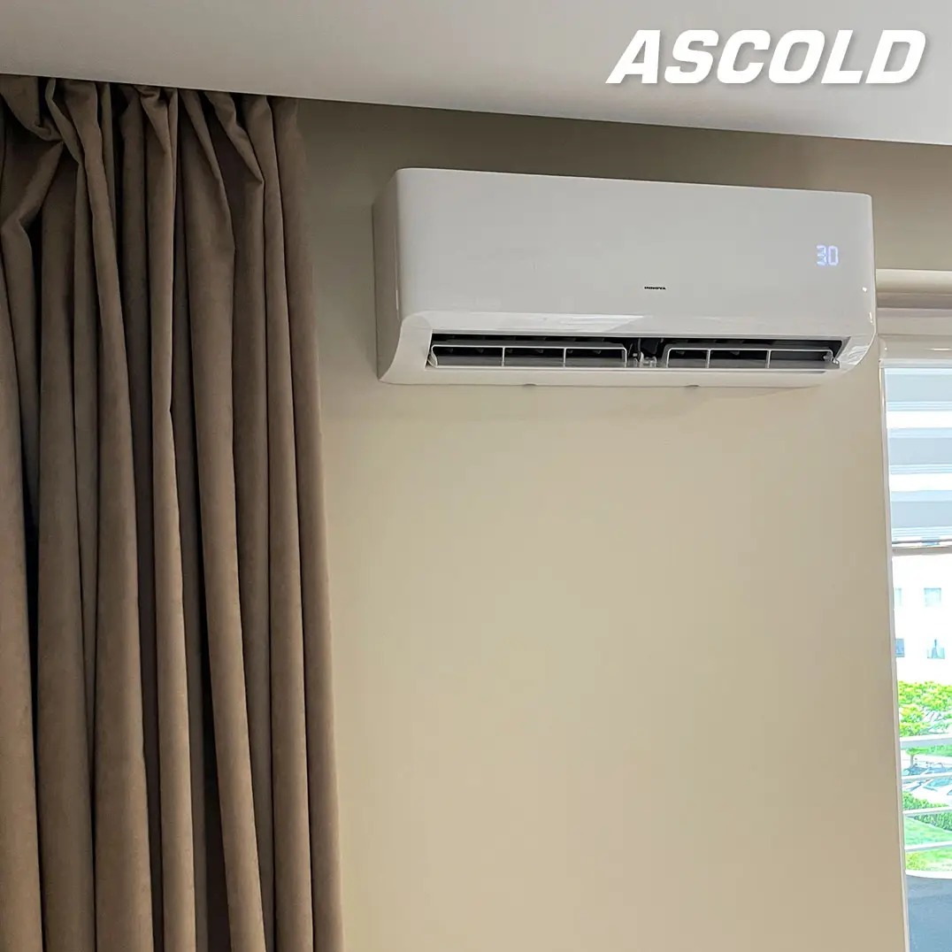 Biała klimatyzacja Ascold na ścianie w pokoju, obok zasłoniętego okna. Na urządzeniu widoczny wyświetlacz z temperaturą 30 stopni.
