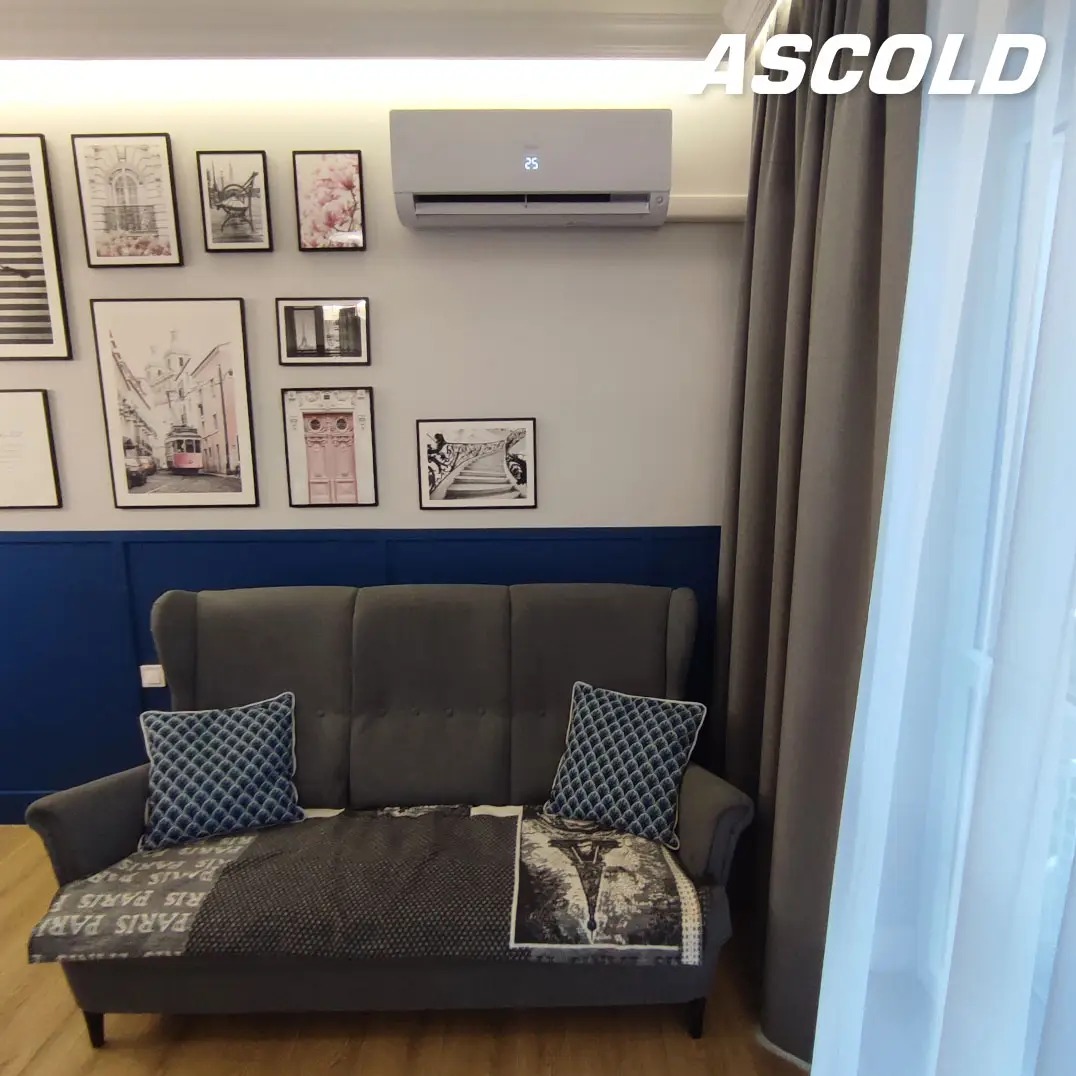 Biały klimatyzator ścienny nad szarą sofą w pokoju z galerią obrazów. Nowoczesne wnętrze z niebieską boazerią i zasłonami.