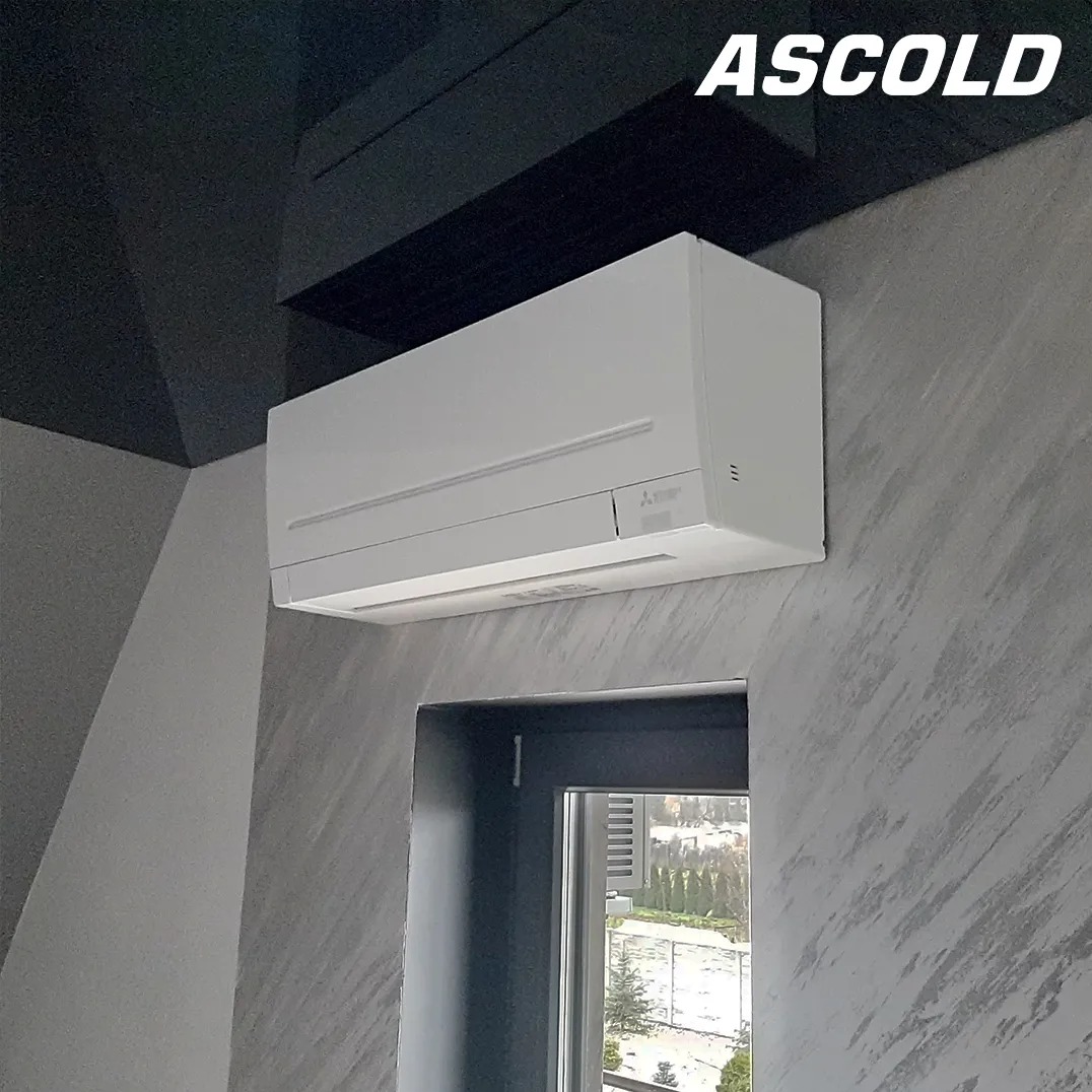 Biały klimatyzator Mitsubishi na ścianie o dekoracyjnej fakturze, widok z boku, okno w tle. Czarny sufit z elementami dekoracyjnymi.