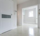 Jasne, przestronne wnętrze z białymi drzwiami z przeszkleniem, widok na pokój z oknem, świeżo wykończona podłoga, minimalistyczny styl.