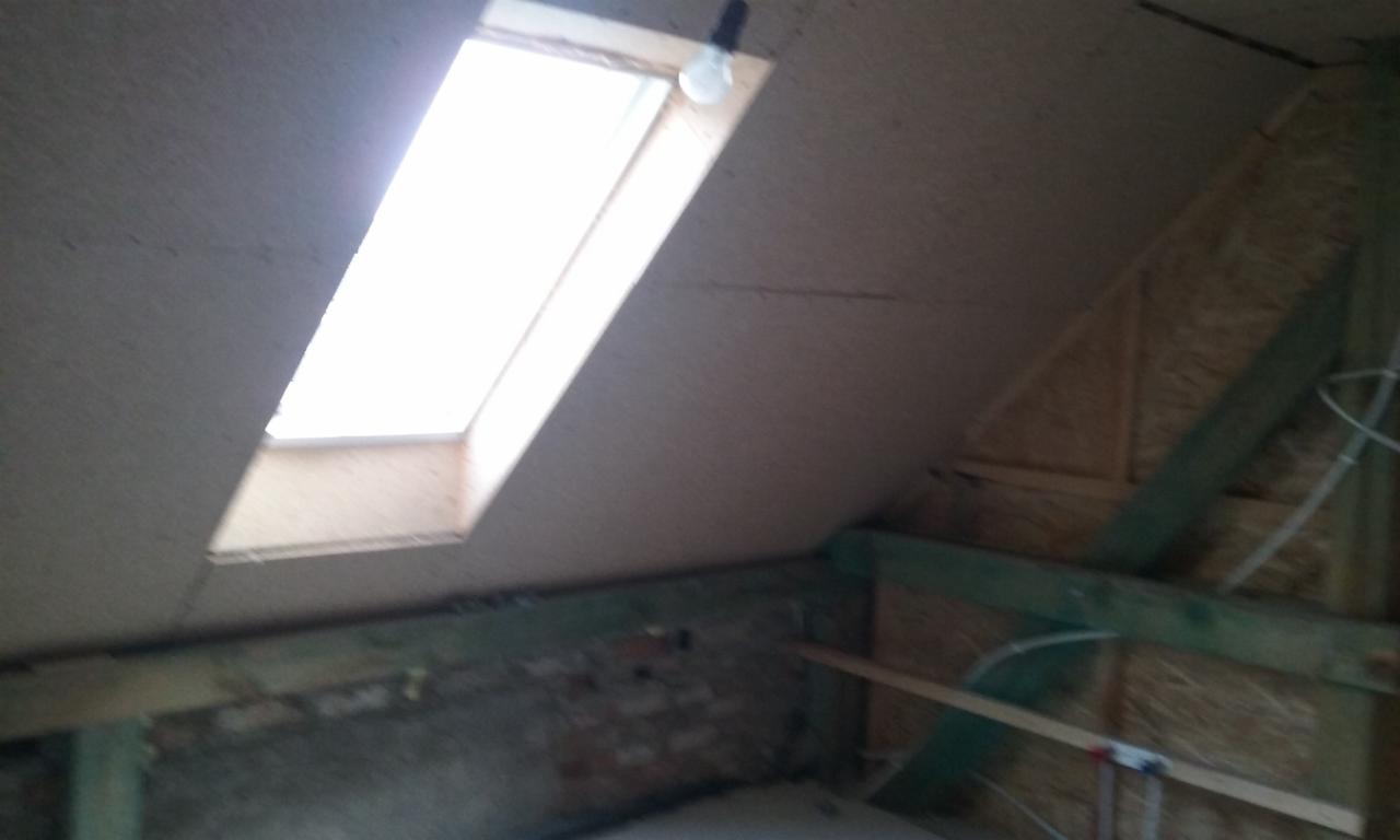 Poddasze w trakcie adaptacji z oknem dachowym i widoczną konstrukcją drewnianą, ściany wyłożone płytą OSB, surowy stan.