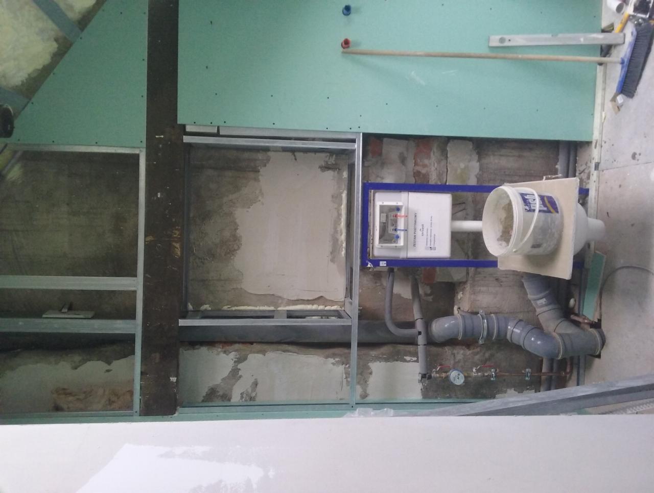 Montaż stelaża podtynkowego WC w trakcie remontu łazienki, widoczne rury kanalizacyjne, fragment ściany z płyt karton-gips oraz metalowa konstrukcja szkieletowa.