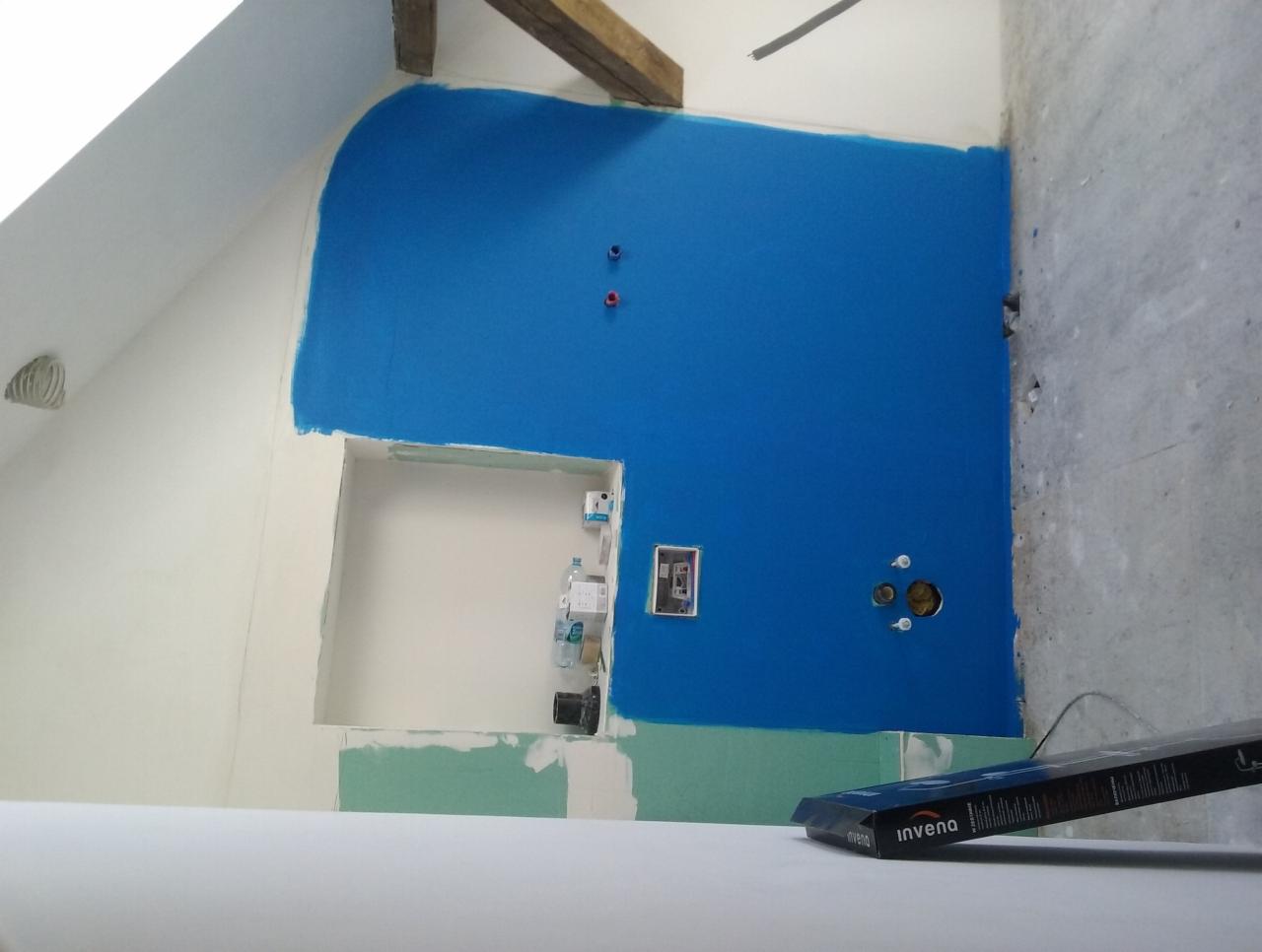 Niebieska hydroizolacja na ścianie w łazience na poddaszu, widoczne przygotowane otwory na instalacje, niezabudowana wnęka i częściowo położone płyty gipsowo-kartonowe.
