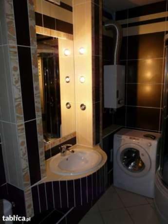 Łazienka z umywalką wbudowaną w szafkę z czarno-białymi paskami, obok pralka i panel z hydromasażem z wbudowanymi punktowymi lampkami.