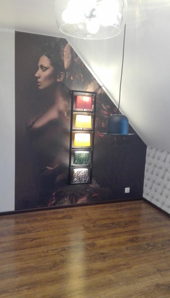 Fototapeta z wizerunkiem kobiety w stylu retro, oświetlona lampą wiszącą i dekoracyjną półką z kolorowymi abażurami, na tle drewnianej podłogi.