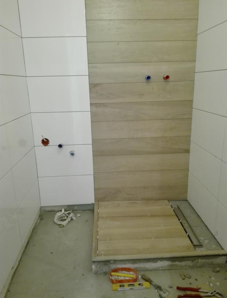 Montaż płytek imitujących drewno na ścianie i podłodze prysznica w łazience w Pelplinie, widoczne narzędzia i poziomica.