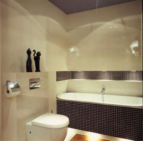 Nowoczesna łazienka z wanną obudowaną czarną mozaiką, podświetleniem LED u dołu, toaletą typu Geberit oraz dekoracyjnymi figurkami kotów na półce.