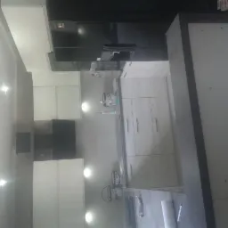 Nowoczesna kuchnia z białymi szafkami z szarymi uchwytami, czarną lodówką i oświetleniem punktowym, widziana z perspektywy szerokokątnej.