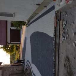 Układanie kostki brukowej na podjeździe przed domem, widoczne wzory z szarej i białej kostki, resztki materiału budowlanego na ziemi.