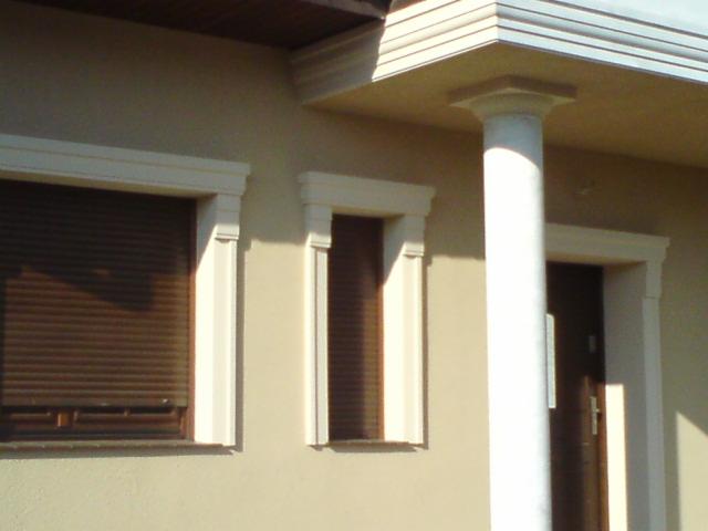 Fragment elewacji domu z oknami z roletami zewnętrznymi, ozdobnymi obramowaniami i kolumną podtrzymującą zadaszenie.