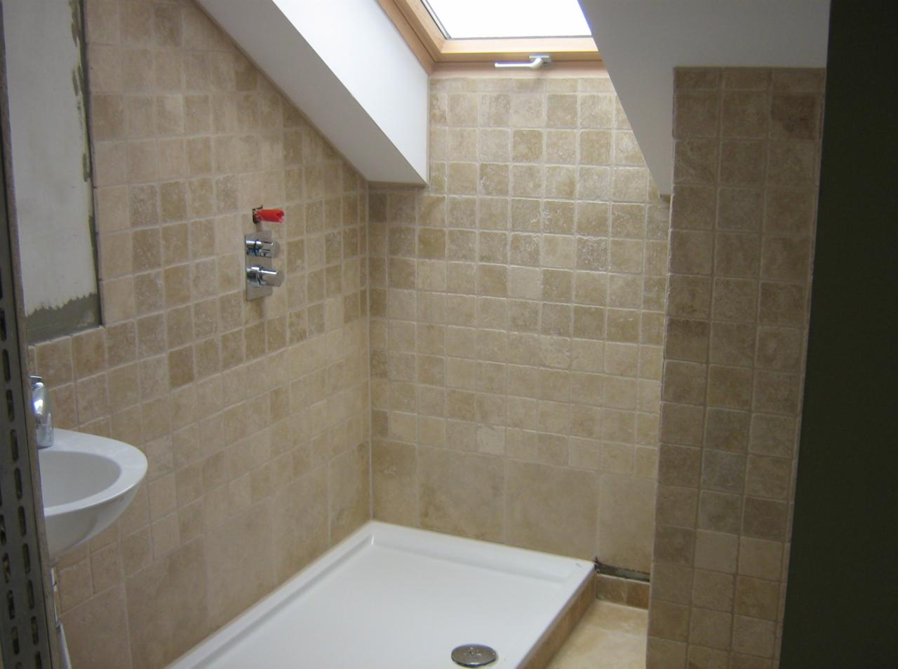 Wykończona łazienka na poddaszu z beżowymi płytkami, białą brodzikiem i umywalką, widoczne okno dachowe i chromowana bateria.