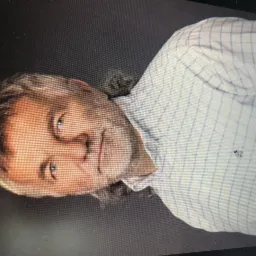 Portret mężczyzny w koszuli w kratę z lekkim uśmiechem, skierowany w lewo.