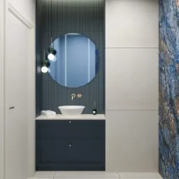 Nowoczesna łazienka z okrągłym lustrem, wiszącymi lampami, białą umywalką na ciemnoniebieskiej szafce i płytkami w odcieniach bieli i niebieskiego.