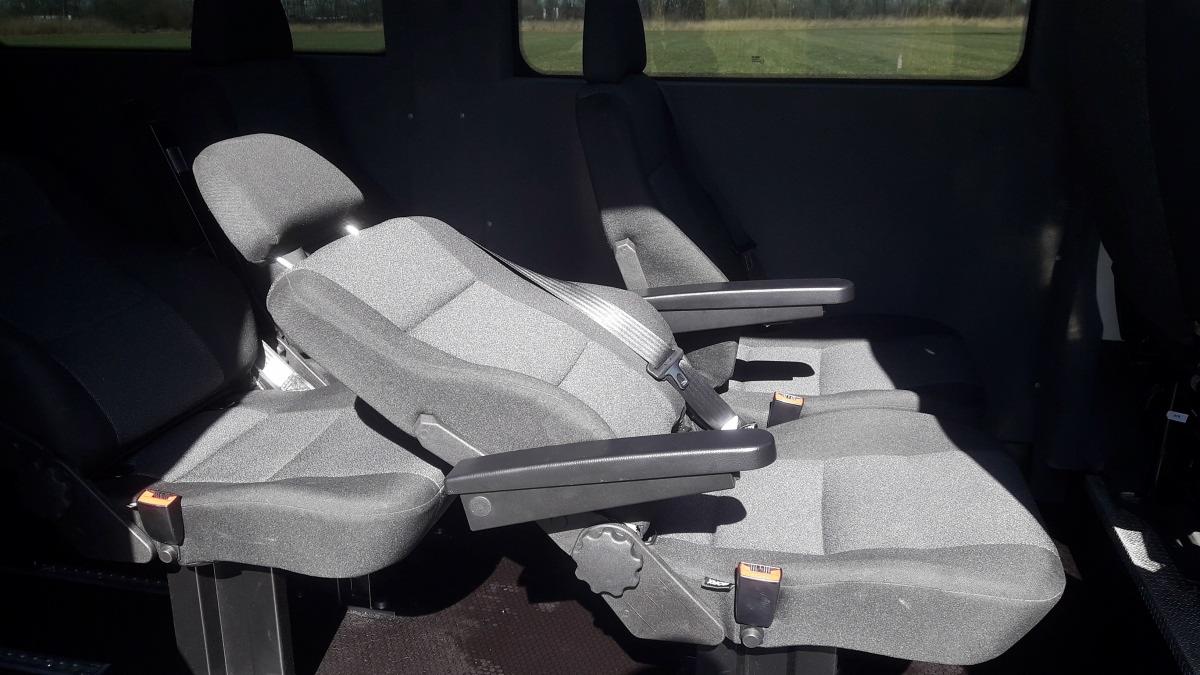 Wnętrze dziewięcioosobowego Fiata Ducato: widok na fotele pasażerskie z regulowanymi podłokietnikami, pasami bezpieczeństwa i widocznym mechanizmem regulacji.