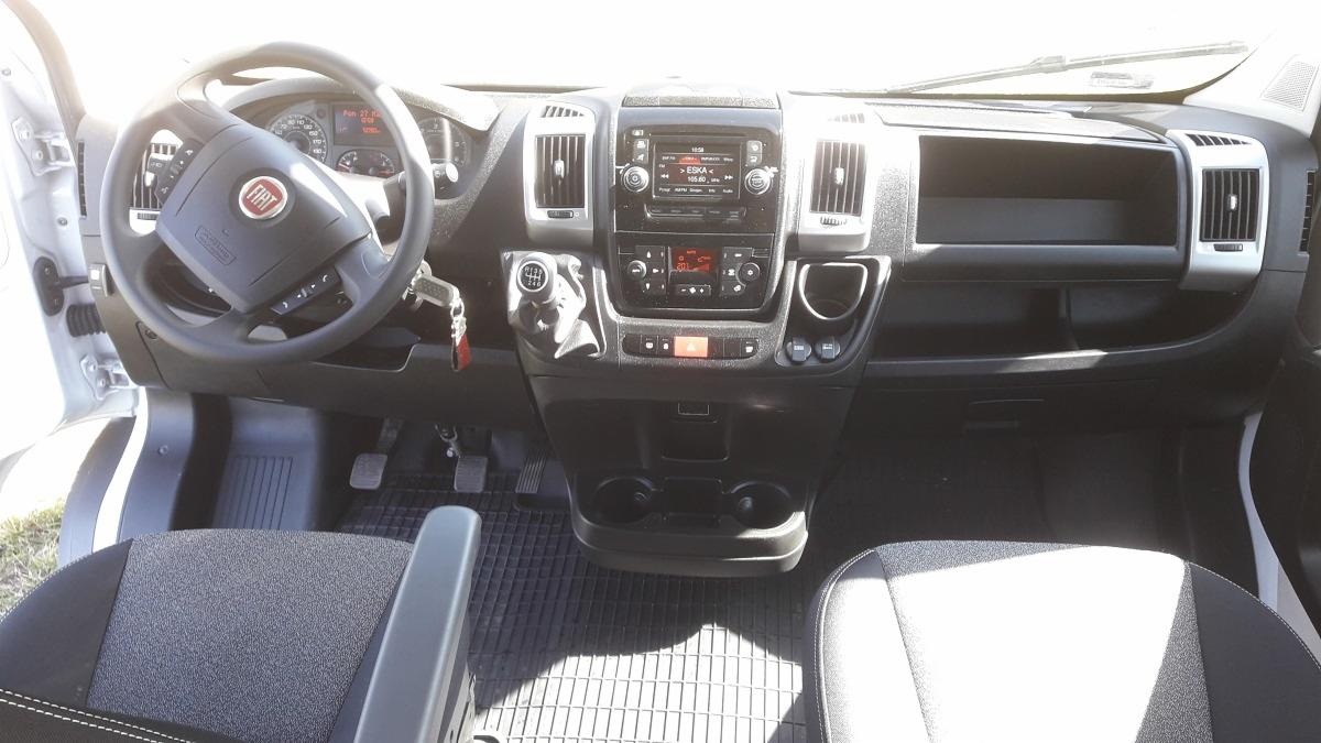 Wnętrze Fiata Ducato: deska rozdzielcza z radiem, kierownica z logo Fiat, kluczyki w stacyjce, widoczne pedały i fragment fotela kierowcy z podłokietnikiem.