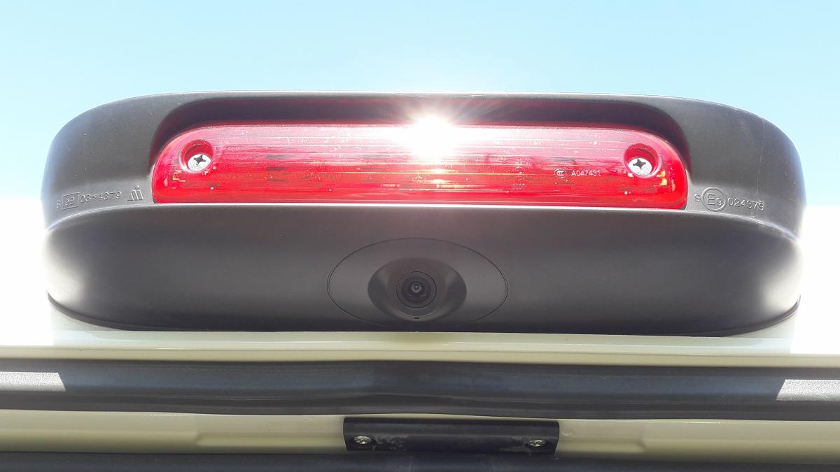 Tylna lampa stop i kamera cofania w samochodzie dostawczym, widoczne oznaczenia homologacyjne i śruby mocujące.