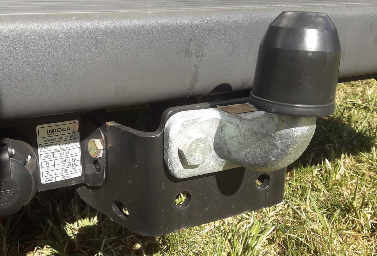 Hak holowniczy z osłoną, zamontowany do pojazdu, widoczna tabliczka znamionowa producenta Imioła z datą produkcji 2016, na tle trawy.