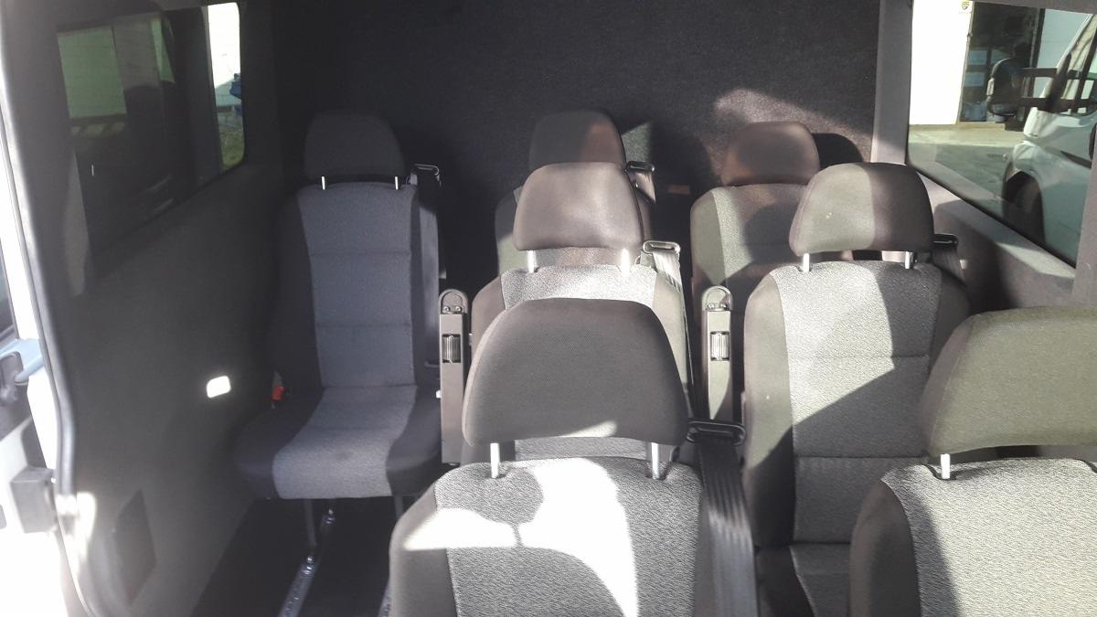 Wnętrze 9-osobowego busa z widocznymi fotelami pasażerów w szarej tapicerce z zagłówkami i pasami bezpieczeństwa, widok z tyłu pojazdu.