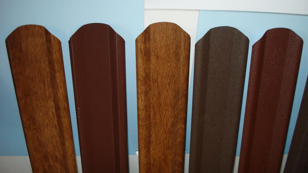 Przekrój przez różne profile metalowe imitujące drewno i gładkie, prezentujące odcienie brązu, używane do budowy ogrodzeń.