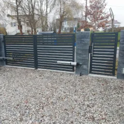 Nowoczesna, pozioma brama wjazdowa z automatyką Somfy, zamontowana na posesji z wysypanym żwirem podjazdem i betonowymi słupkami.